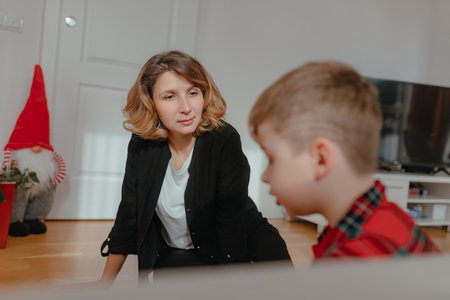Woman leaning forward observing boy during quiet moment floor wooden interior soft daylight red plaid pajamas balanced framing parentâchild interaction domestic atmosphere.の写真素材