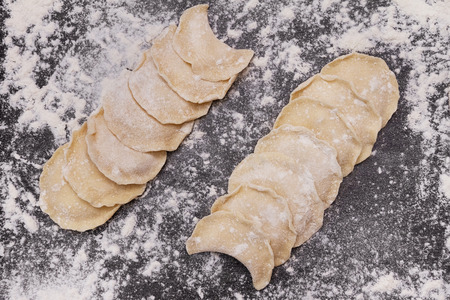 Dumplings vareniki lie in two rows on black table sprinkled with flourの写真素材