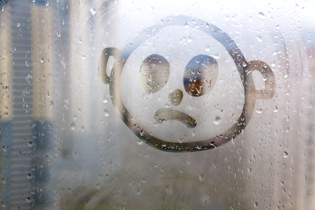 Foggy glass on window with drawn sad face concept photo with copyspaceの写真素材