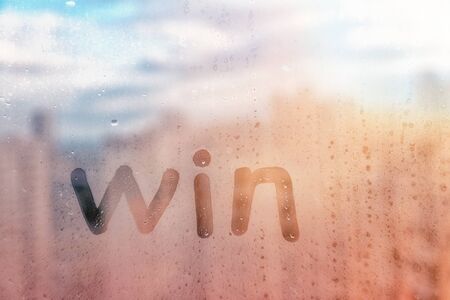 Foggy glass on window with written finger word Win concept photo with copy space on red sunrise backgroundの写真素材