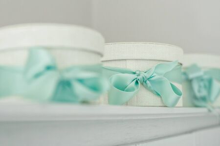 three white boxes of natural fabric tied with a blue bow stand on a gray surface