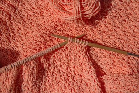 Coral cotton cardigan, crocheted close-up with loops on wooden bamboo natural knitting needles with...