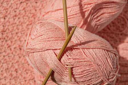 two skeins of coral yarn with bamboo circular knitting needles on cotton knitted fabric