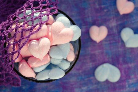 pastel pink and blue heart-shaped meringue cakes in a glass cup on a lilac background with purple stripe, natural violet bag with cotton mesh.の写真素材