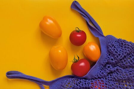 two red and three yellow tomatoes are in purple cotton eco bag on orange background on leftの写真素材