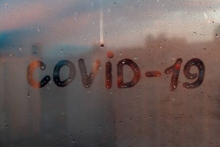 Foggy glass on window with written finger word yellow color Covid-19 concept photo with copy space on blue red backgroundの写真素材