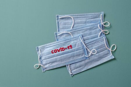 four new disposable medical masks on one mask with the red word covid-19 lie on green surface, pandemicの写真素材