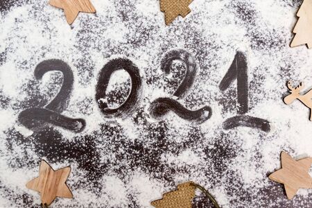 Arabic numerals 2021 painted on white flour on black table and and wooden flat natural christmas...