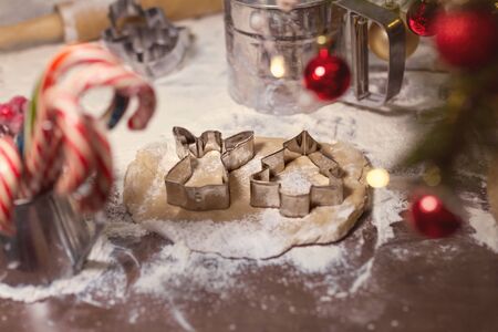 cookie cutters and angel lie on shortcrust pastry on table with flour, red candy and red christmas...