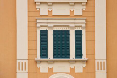 green wooden window with shutters in white frame on the yellow wall