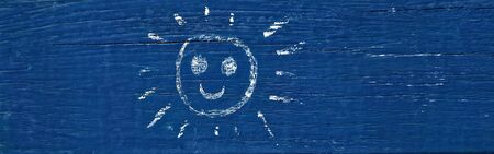 smiling sun painted with yellow chalk on old blue wooden board. The positive faceの写真素材