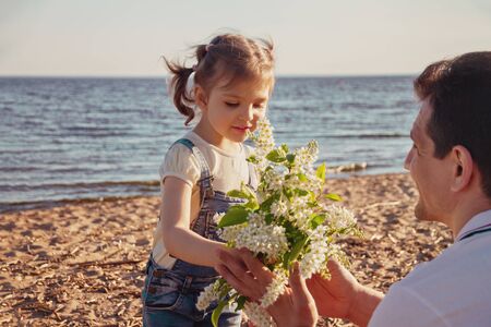 little girl runs to dad with bouquet of flowers on sunny day beach in summer