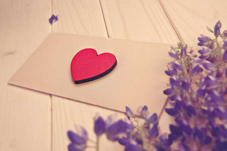 little red heart lies on brown envelope on rustic table with flowers lupine copy space