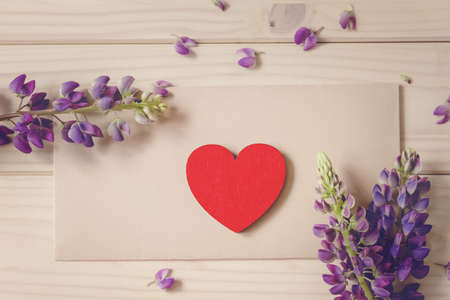 flat lay red vintage wood heart lies on craft envelope on rustic table with bouquet of flowers lupine, concept love, messageの写真素材