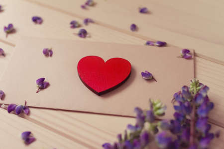 brown vintage envelope with craft red heart in perspective on wooden table with bouquet of flowers lupine diagonallyの写真素材