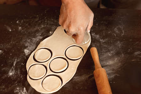 dumplings manufacturing process: male hand in raw dough squeezes circle