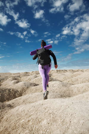woman solo tourist running in jump, rear view on hill area in sportswear and with backpack looking into distance on sunny day, concept of healthy lifestyle, sports, overcoming obstaclesの写真素材