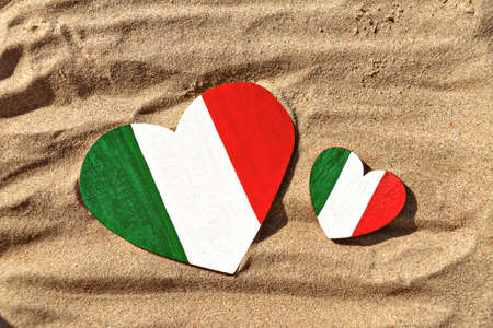 two wooden hearts big and small painted in colors of the flag of Italy green, white and red lies on the golden sand on the beachの写真素材