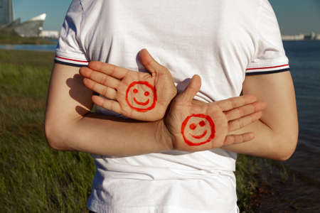 male two palms with paint red face and smile behind the back white t-shirt on beachの写真素材