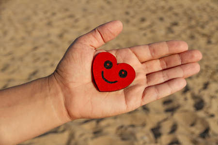 male palm with painted black smiling face on red heart and yellow sand, smile day conceptの写真素材