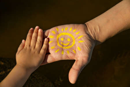 childrens palm on mans hand with yellow smiling sun stretches out his hand to childs palmの写真素材