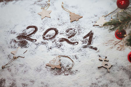 numbers 2021 paint handwritten on flour brown table and wooden flat christmas tree toys around with...