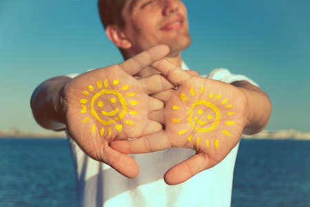 mens hand with paint yellow sun face and smile against blue sky, copy space, close up