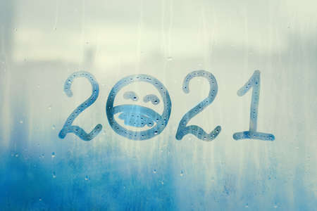 hahdmade painted numbers 2021 with sad face with closed eyes in protective medical mask on splashed...