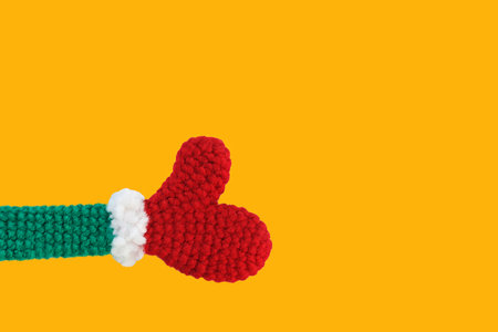 one knitted new year, christmas toy red mittens on green sleeves with white cuffs shows right thumbs up on yellow backgtound, isolate, copy spaceの写真素材