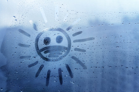 Hand drawn sad face against virus painted on window flooded with raindrops on blue backgroundの写真素材
