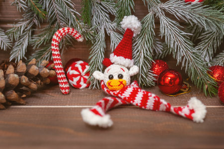 knitted toy white bull head in christmas cap and scarf with fir branches and decor on wooden brown...