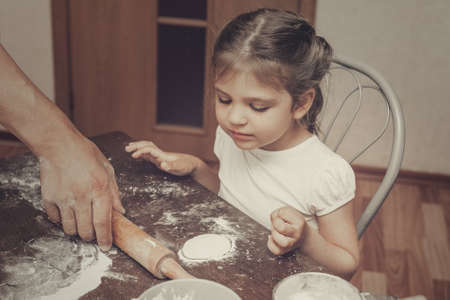 small child girl 3 years old sits at the table floured in kitchen and sculpted out of dough, film noise, retroの写真素材