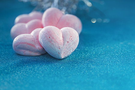 pink sweet meringue hearts on blue sparkling background, copy space