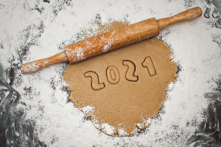 Arabic numerals 2021 painted on white flour on black table and rolling pin horizontally down, close...