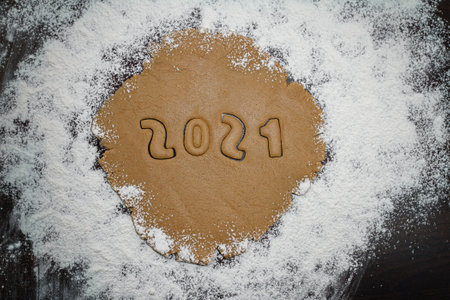 Arabic numerals 2021 cut from rolled raw brown cookie dough on white flour, flat layの写真素材