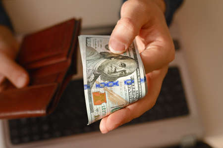 one hundred dollar banknotes in bundle protruded from leather brown wallet in mens hand on...