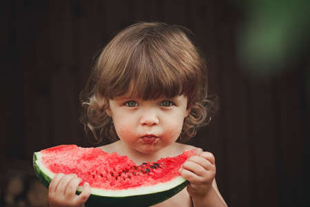 2 years old child holds a piece of ripe red watermelon with seeds close-up, selective focusの写真素材