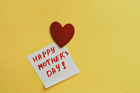 two piece of paper for notes with words Happy Mother's Day and red wooden heart on yellow background, selective focus, copy spaceの写真素材