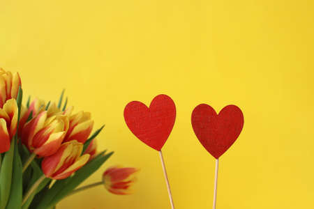 twain wooden red heart and bouquet of yellow pink tulips on yellow background, copy space