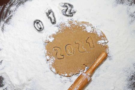 Arabic numerals 2021 cut from rolled raw brown cookie dough on white flour, rolling pin with metal cookie cutters, flat layの写真素材