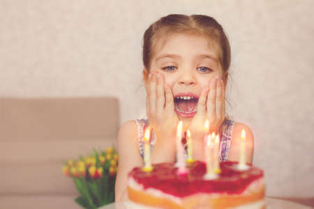 3 year old girl emotionally looks at the candles on the cake at home