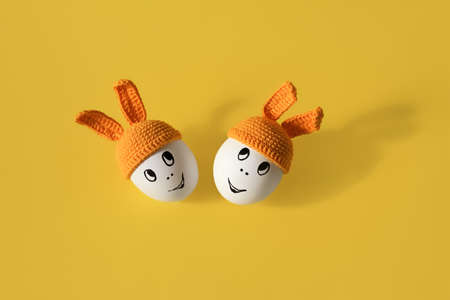 two white eggs in beanie with rabbit ears and cheerful faces on yellow background