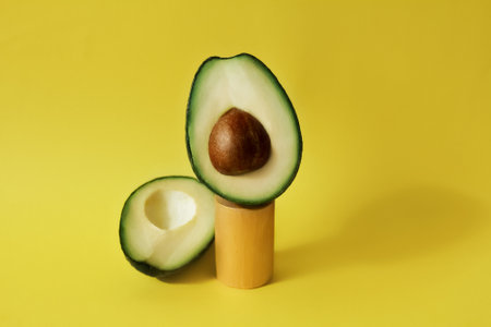 cut avocado fruit on celendric podium and yellow backgroundの写真素材