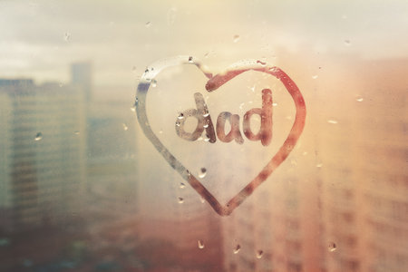 Foggy glass on window with written finger word dad my in heart shape on sunset overcast wet windowの写真素材
