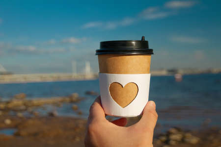 brown natural paper cup of ground coffee espresso with carved white heart in woman's hand on...