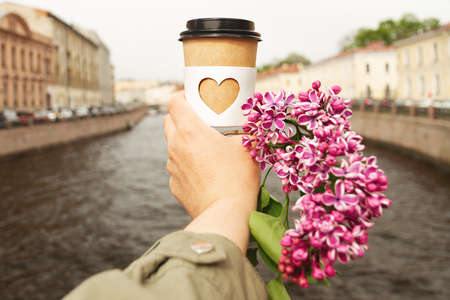 paper cup of natural coffee in womans palm on background of river Griboyedov Canal in St. Petersburgの写真素材