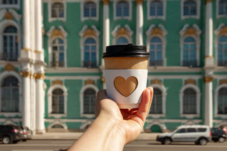 paper cup of natural coffee with carved white heart in womans palm on background of Winter palace l in St. Petersburgの写真素材