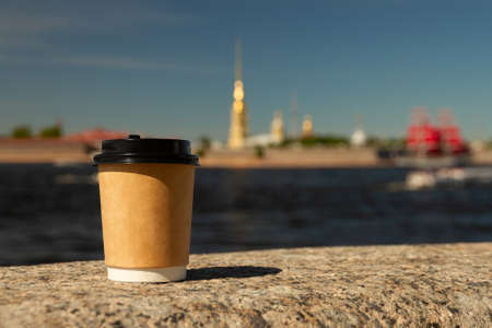 brown natural paper cup of ground coffee on granite embankment of Neva River against background of Peter and Paul Fortress in blur in St. Petersburg, Russia on sunny day, copy spaceの写真素材