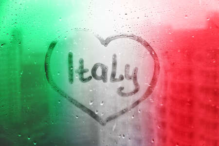 Handwritten word Italy in heart shape on misted window with raindrops in colors of italian flagの写真素材