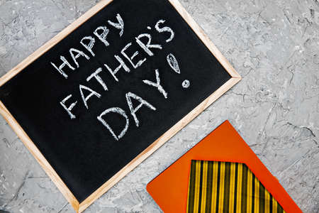 congratulations text Happy fathers day on chalk board with orange diary and yellow tie on gray concrete backgroundの写真素材